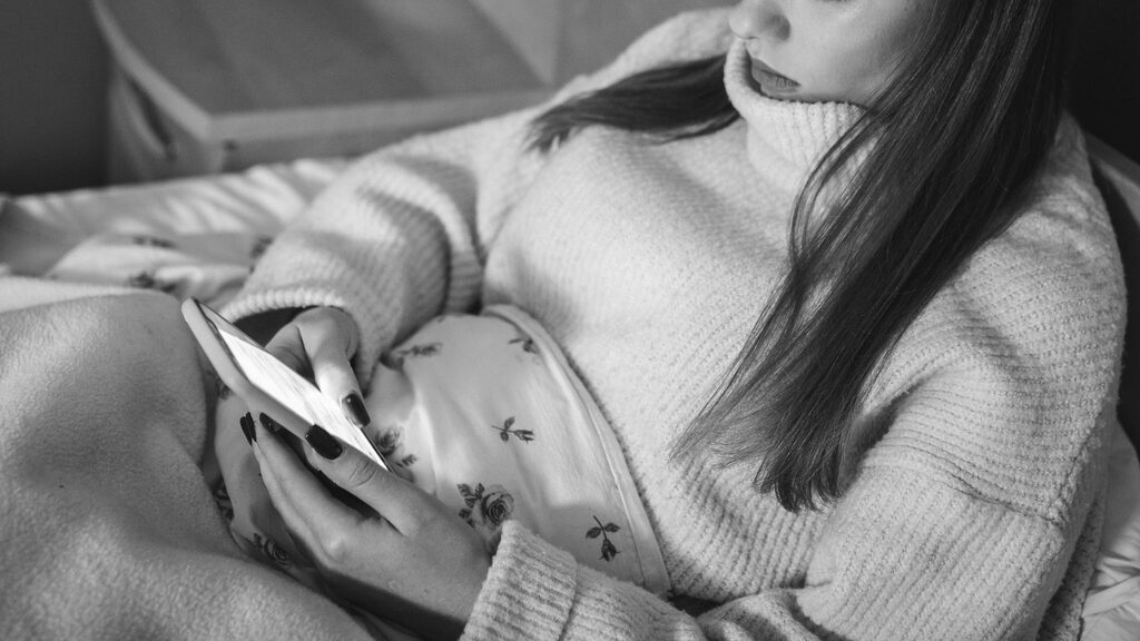 Una donna avvolta in una calda maglia e una coperta è seduta comodamente mentre tiene uno smartphone.