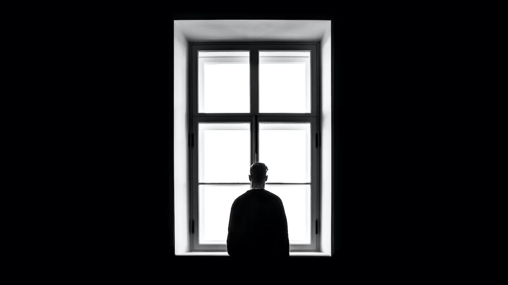 Una potente immagine in bianco e nero cattura il profilo di una persona in piedi davanti a una finestra luminosa.